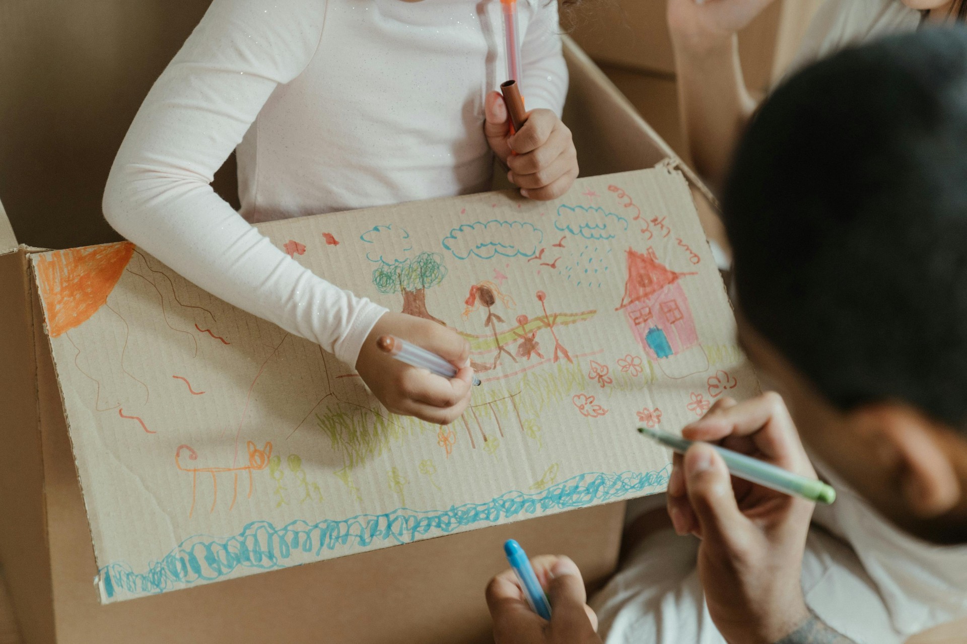 Crianças e adulto desenhando juntos em caixa de papelão